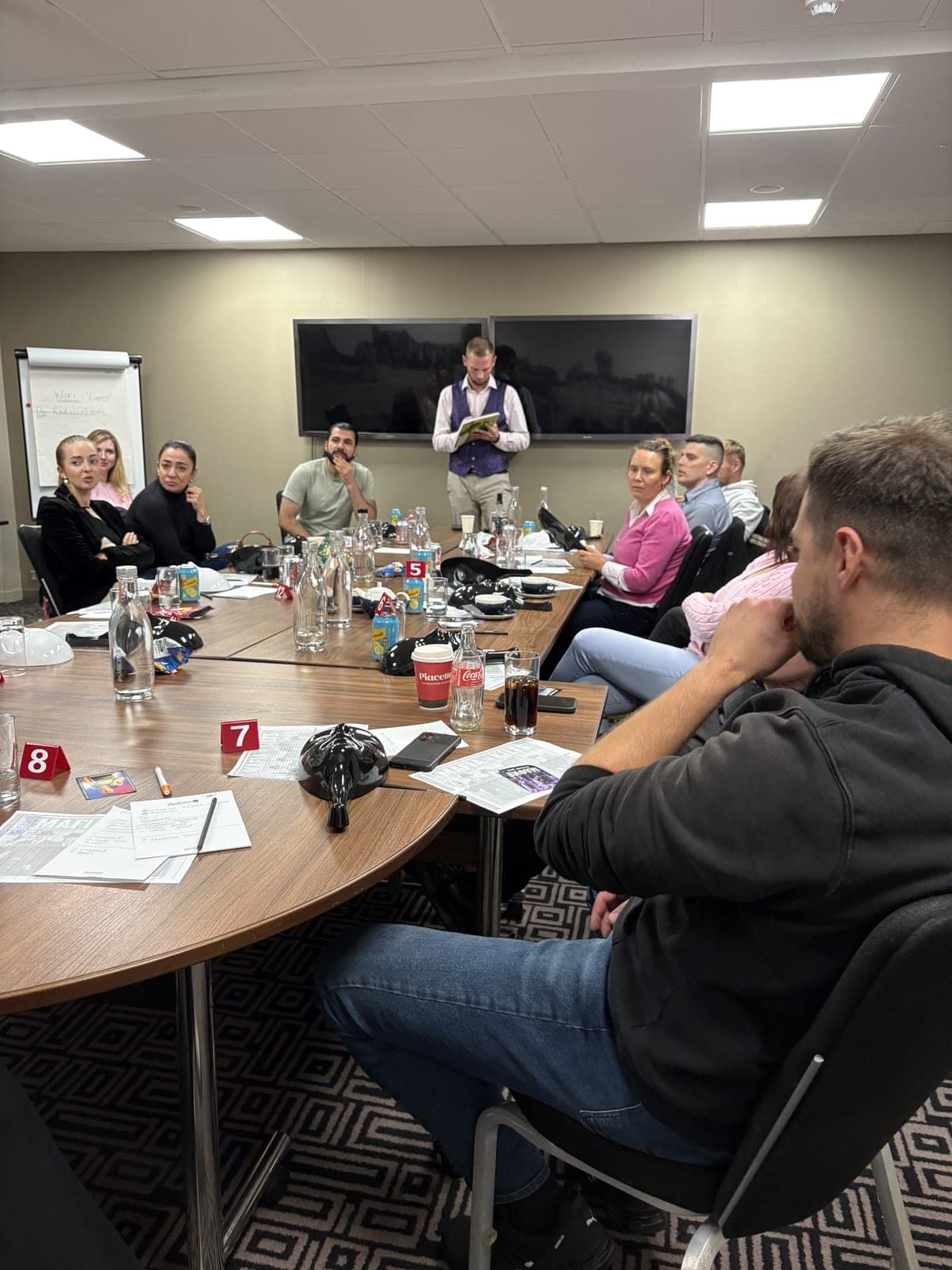 A host running a Mafia Kilty game for a corporate team around the table